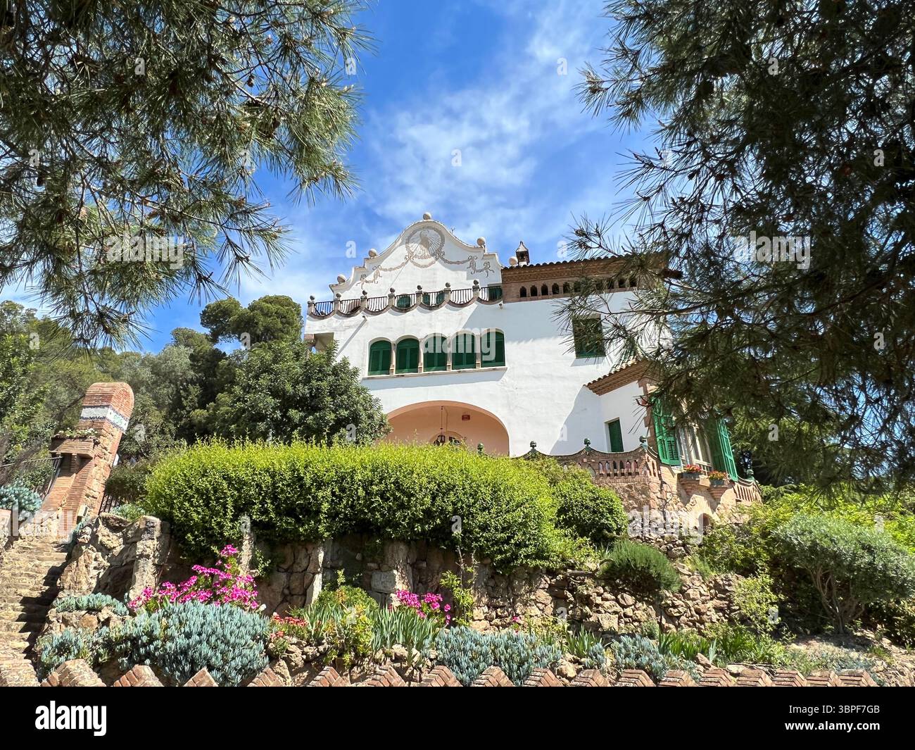 A charming white building surrounded by lush greenery and a bright blue sky, an ideal scenic view. Barcelona, Spain - Smartphone Captured Stock Image