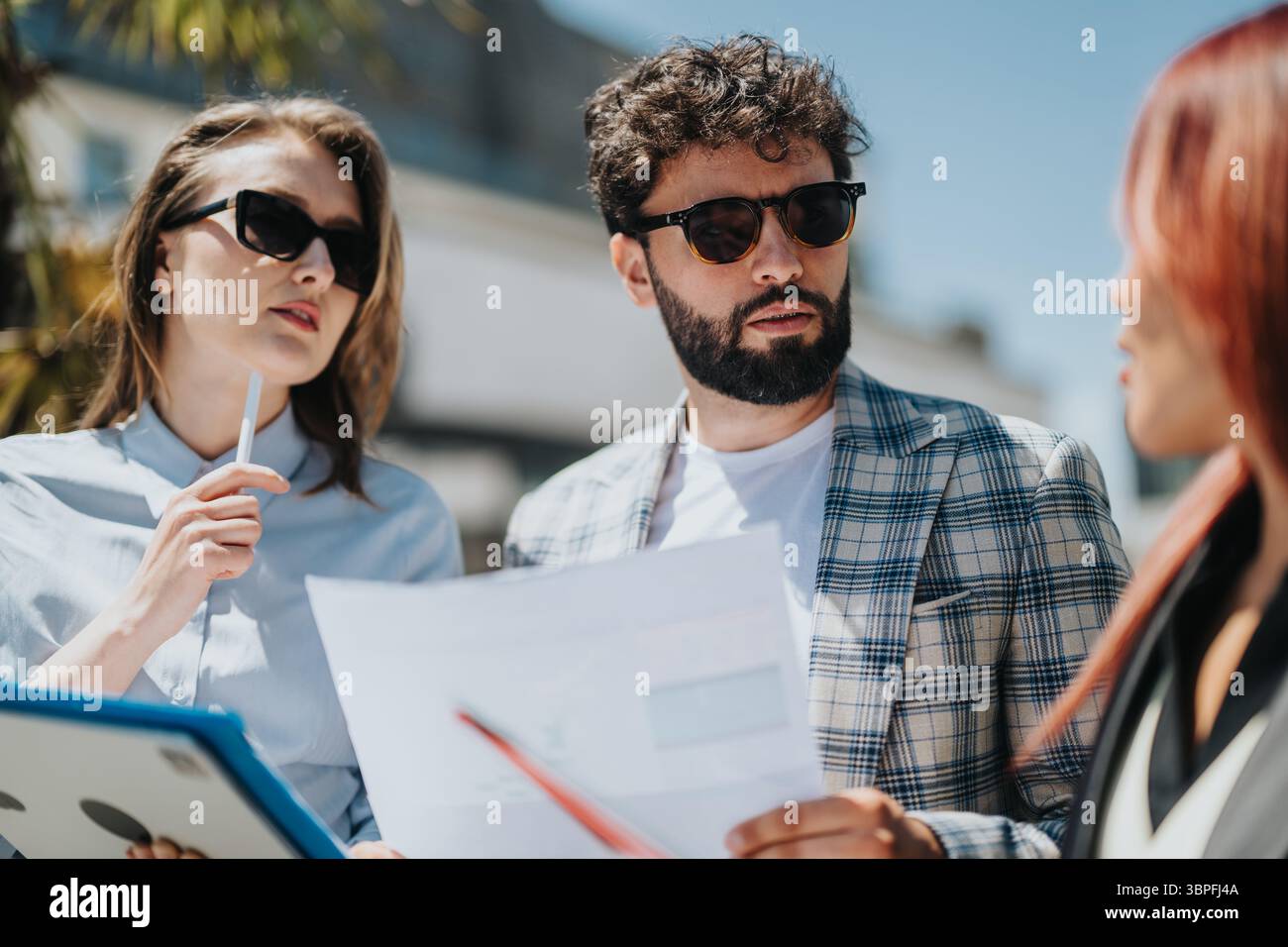 Group of business professionals discussing projects outdoors in bright sunlight Stock Photo