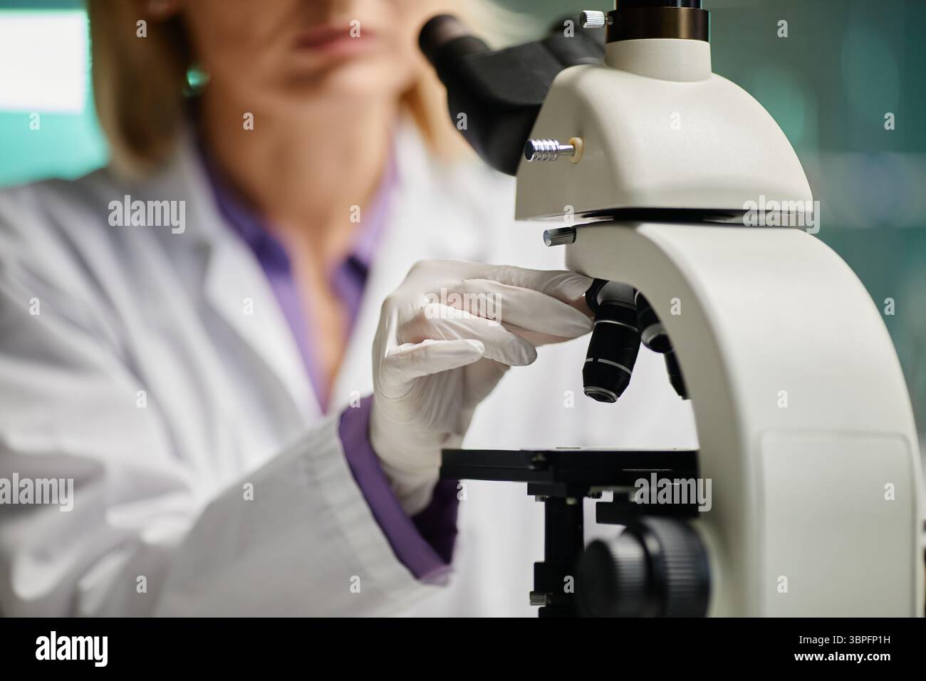 Caucasian middle aged woman adjusting microscope in scientific laboratory, wearing lab coat and gloves, focusing on specimen slide, conducting research or analysis in professional environment Stock Photo