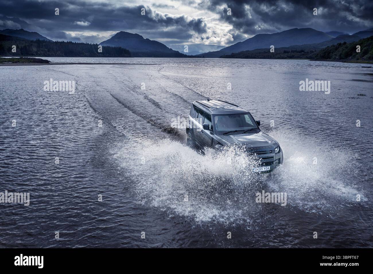 Brooding Estate Aerial view of a Land Rover Defender carving through the dark, rippling ...