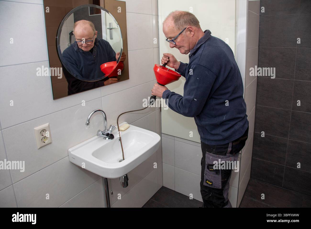 Netherlands, a plumber is using a handheld drain auger or 'plumber's snake'. Handheld drain augers are typically designed to clean portions of a drain Stock Photo