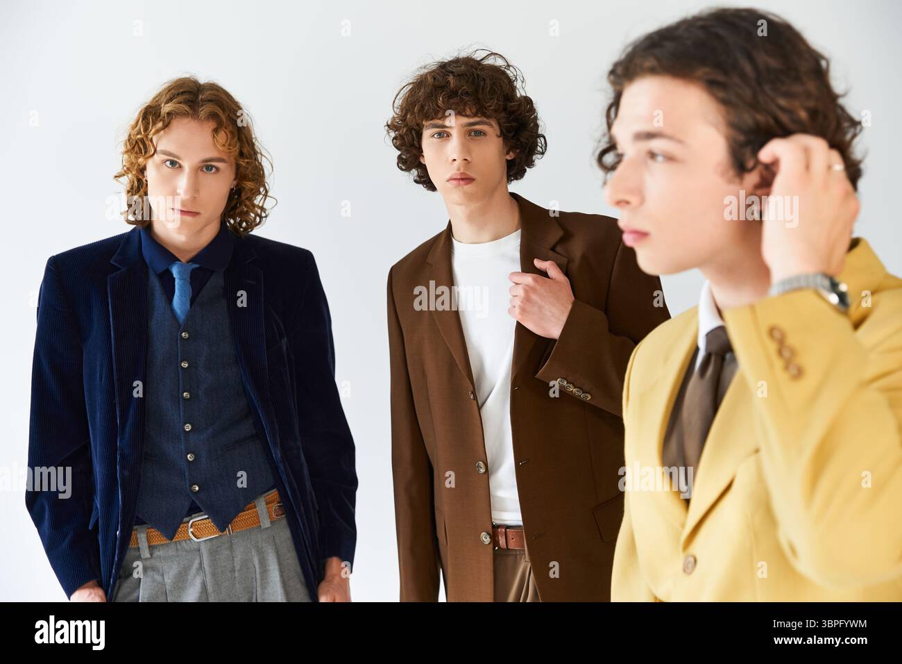 Three young men display unique fashion styles while posing confidently in a bright space. Stock Photo