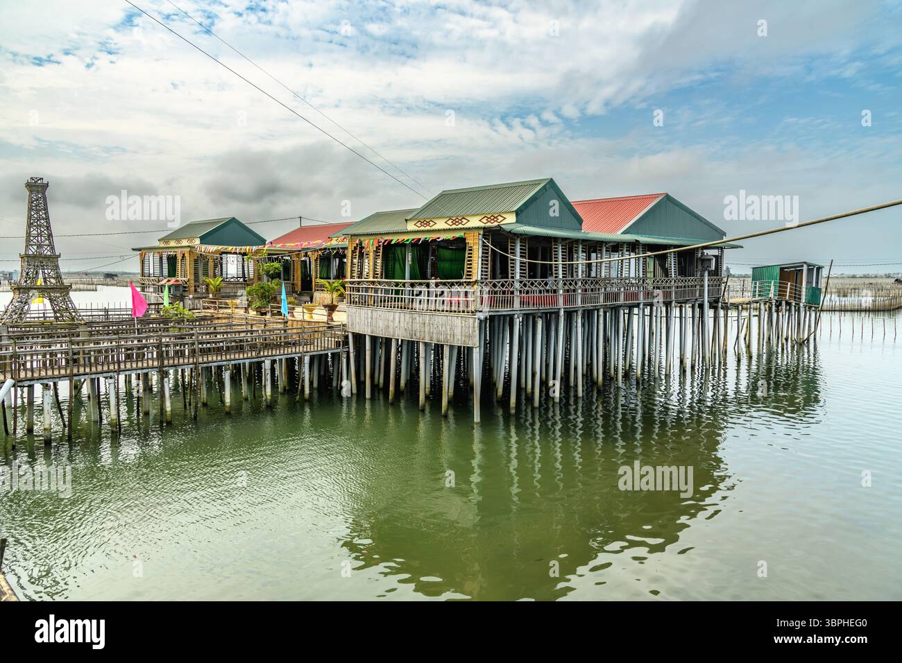 A picturesque view of stilt houses rising from a calm, green-tinged ...