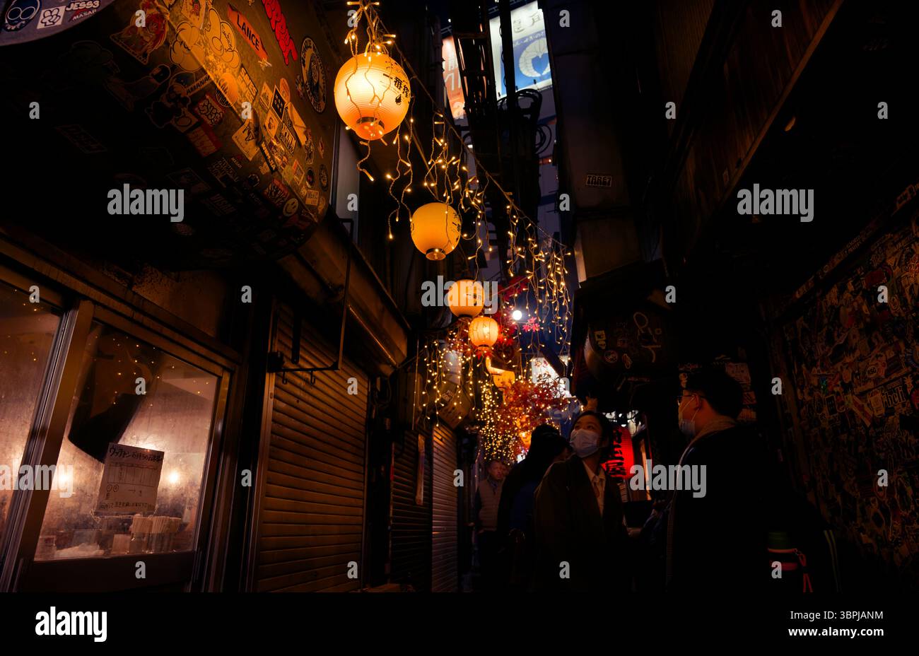 Warm lanterns and string lights illuminate a narrow alley in Tokyo as people explore the lively bar and food scene at night Stock Photo