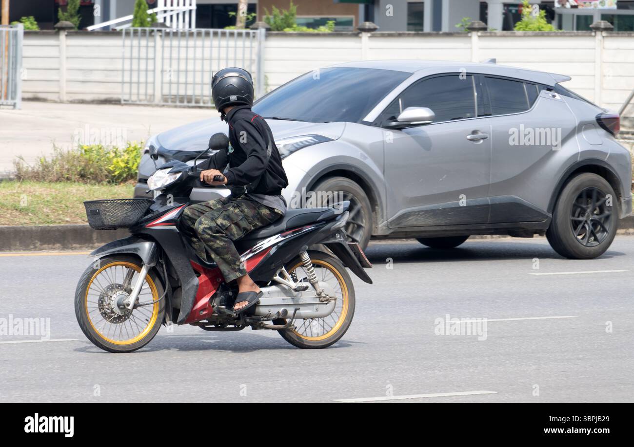 A man riding a motorcycle turns around to look at a car he is passing, Thailand Stock Photo
