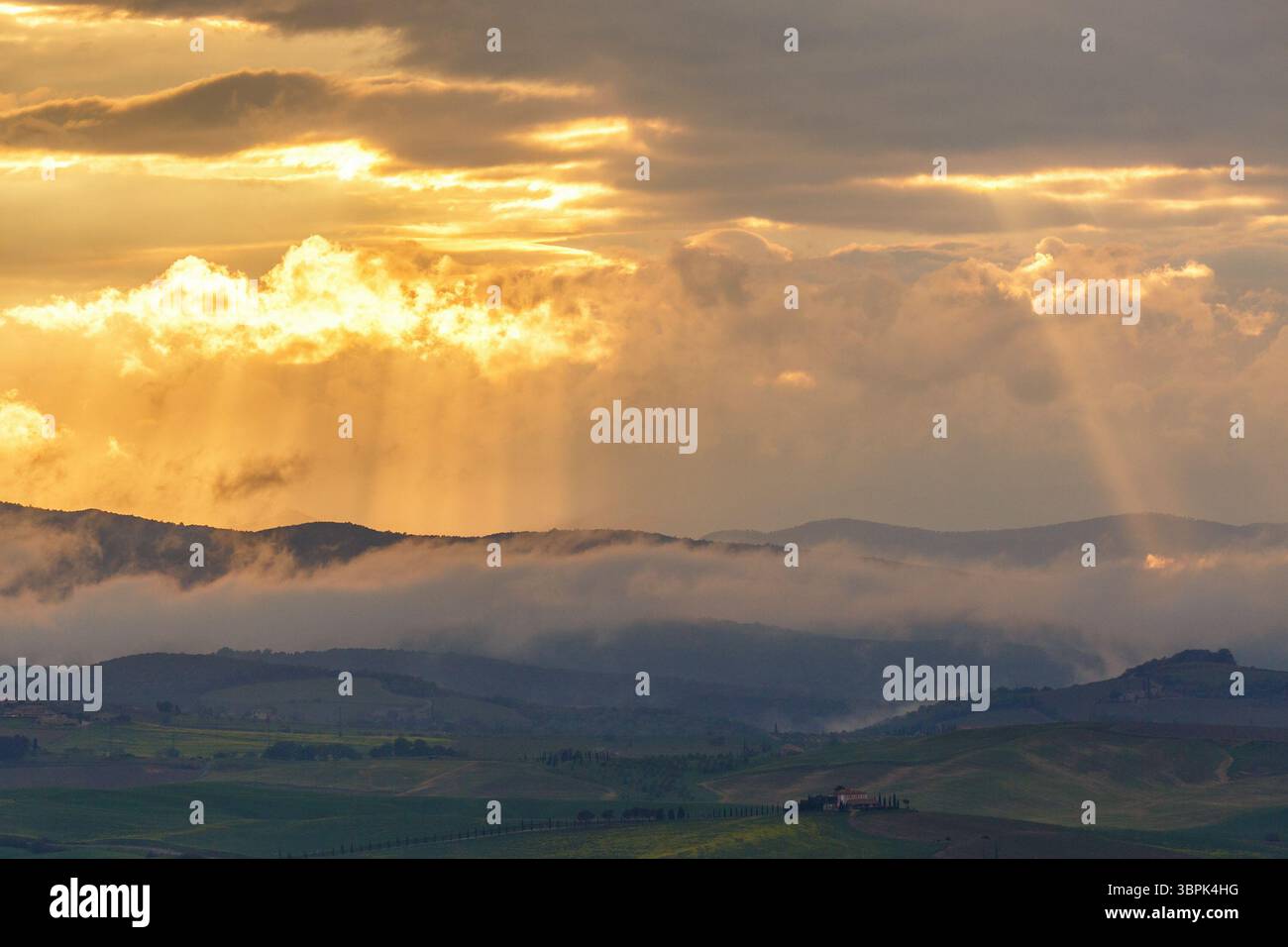 Sunset over the mountains with sun rays and low clouds Stock Photo