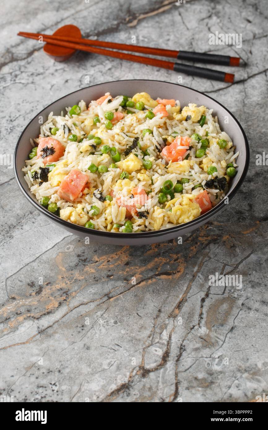 Stir fry rice with salmon, egg, green peas, onion and seaweed close-up in bowl on table. Vertical Stock Photo