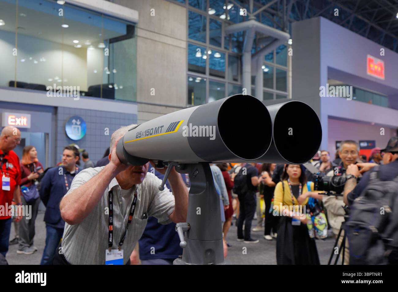 A person looks through a pair of Fujinon 25x150 MT binoculars at a photography trade show Stock Photo