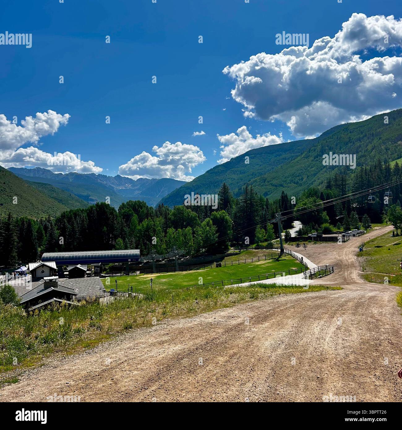 Ski Resort Base Area in Summer with Mountain Roads and Active Chairlift. A wide dirt road winding down through a grassy ski resort base. - Smartphone Captured Stock Image