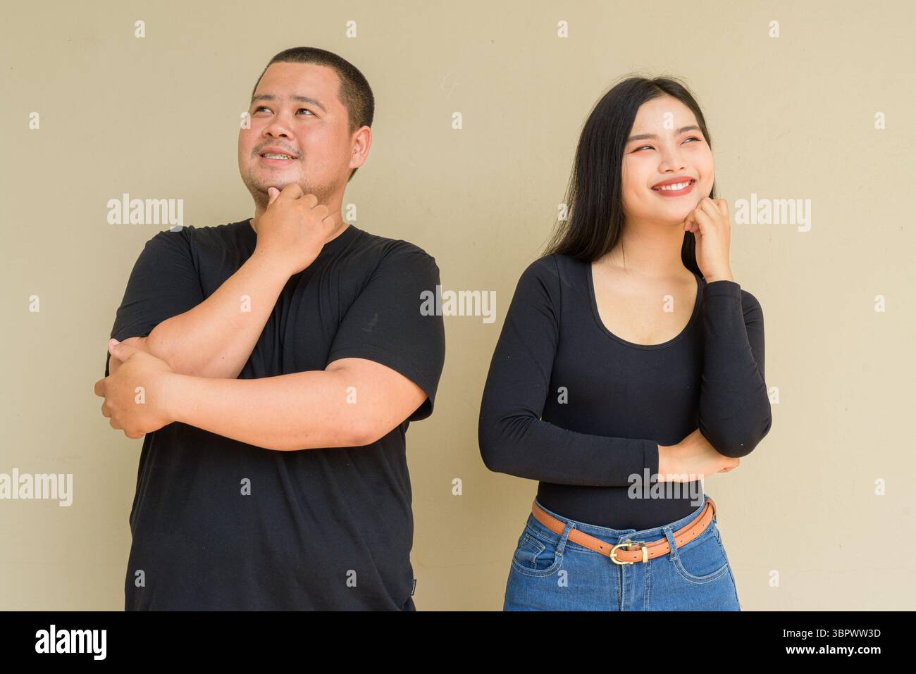 Portrait of young Asian couple against plain wall background thinking Stock Photo