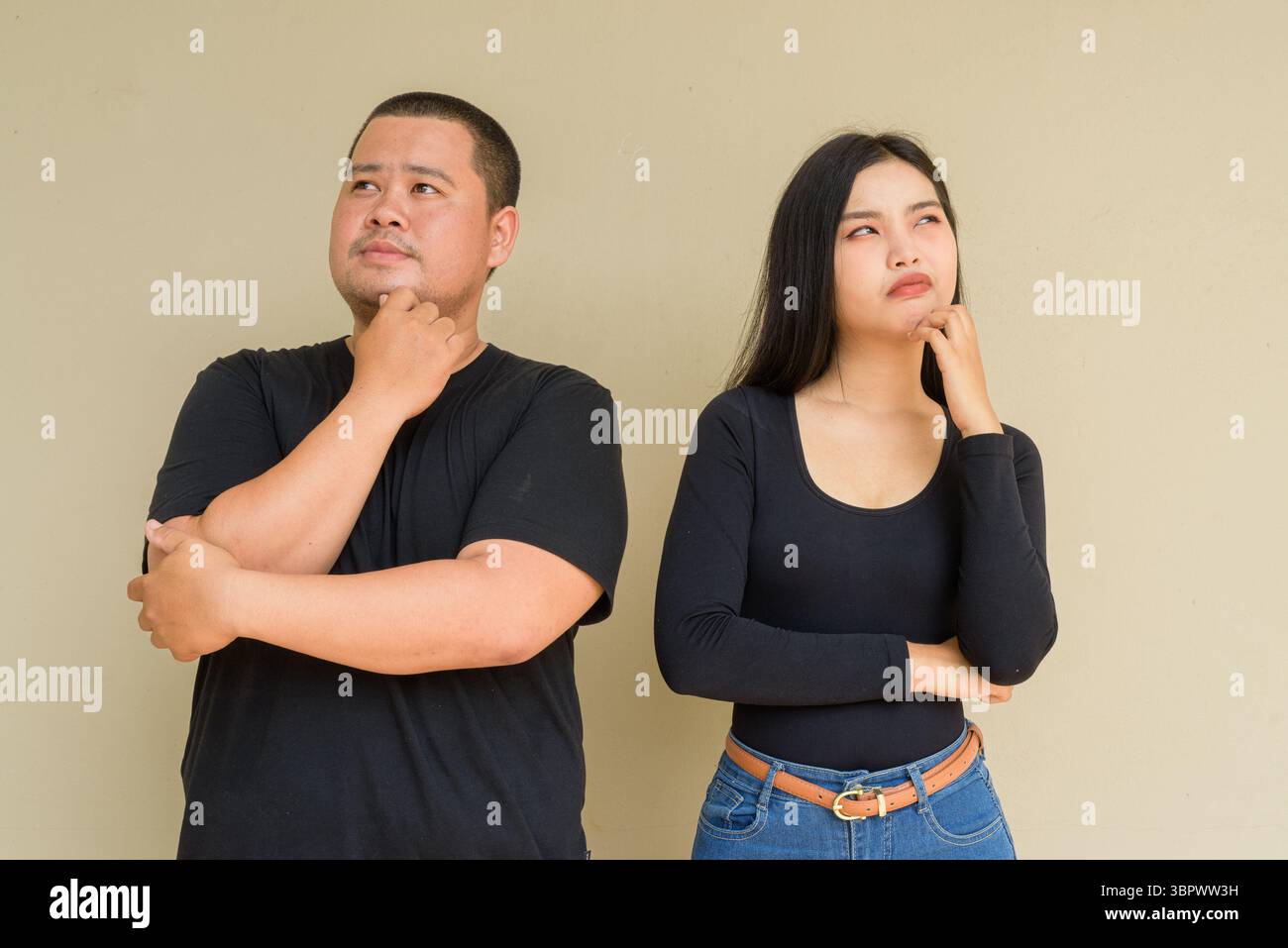 Portrait of young Asian couple against plain wall background thinking Stock Photo