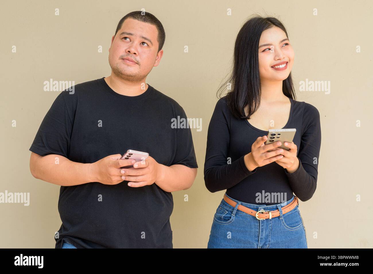 Portrait of young Asian couple against plain wall background Stock Photo
