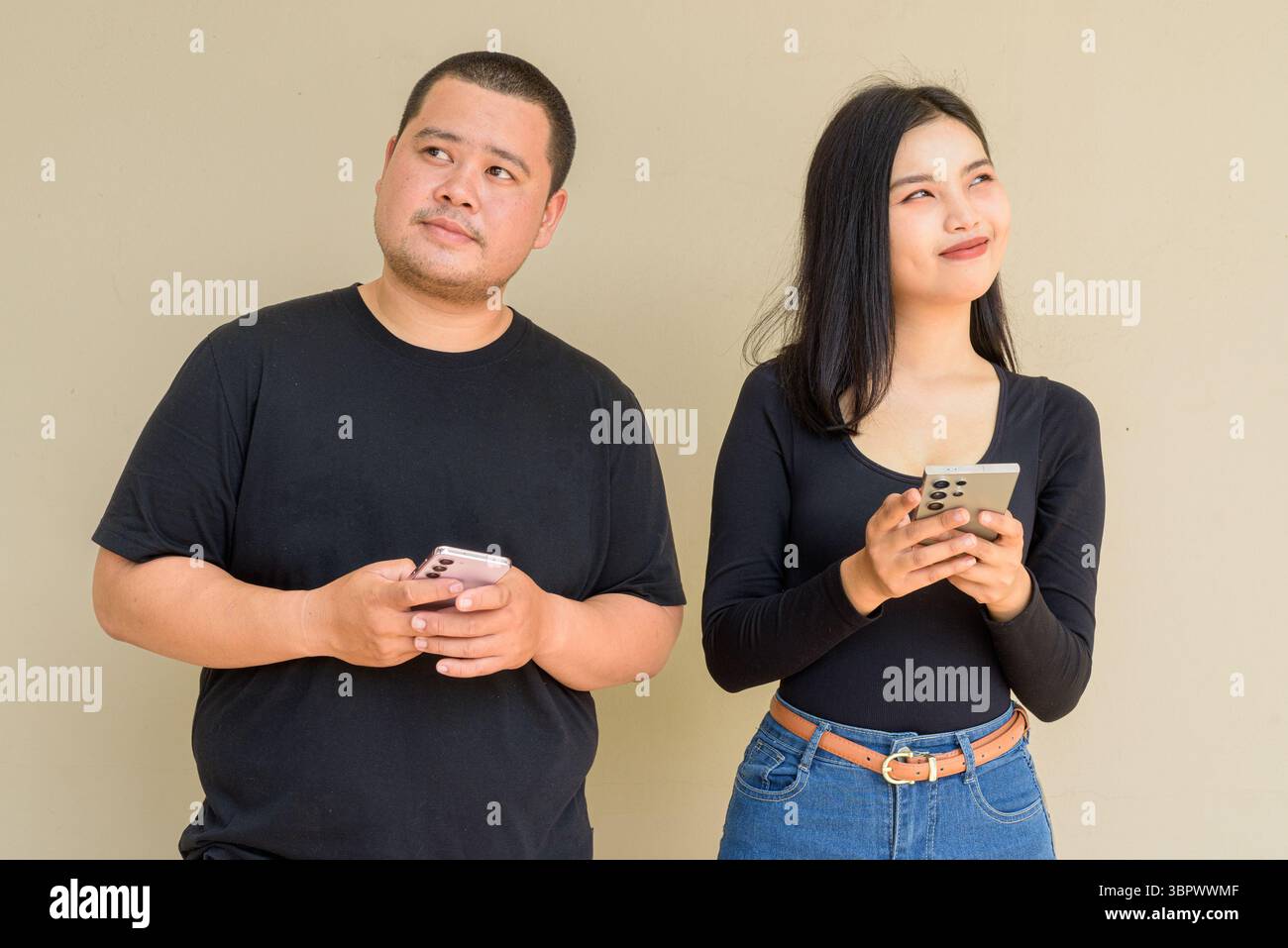 Portrait of young Asian couple against plain wall background Stock Photo
