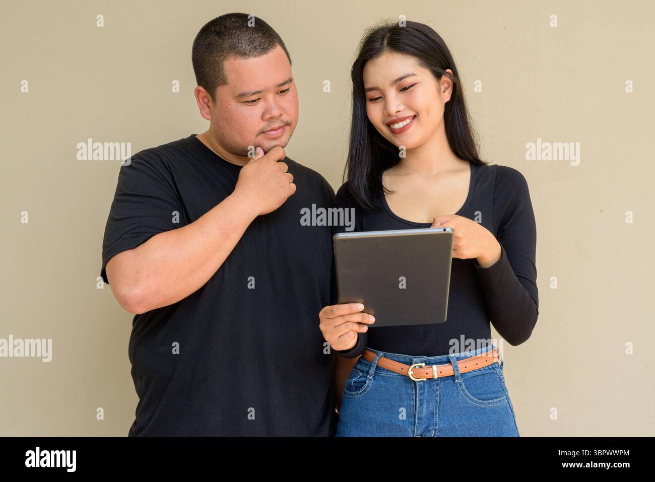 Portrait of young Asian couple against plain wall background Stock Photo