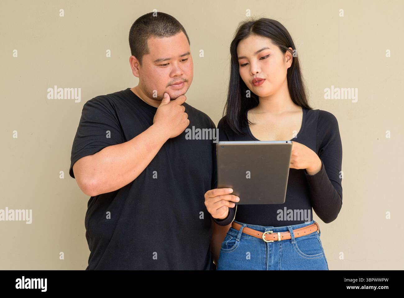 Portrait of young Asian couple against plain wall background Stock Photo