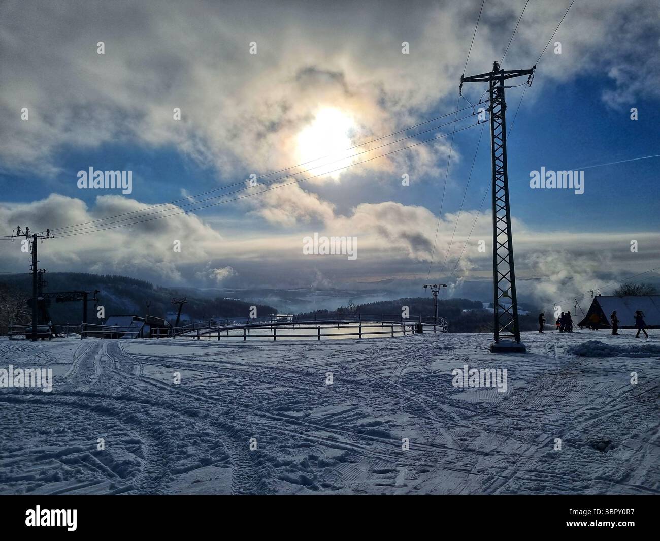 A large power pylon silhouetted against a dramatic sunlit sky, creating a powerful contrast between technology and nature in a snowy Czech landscape. - Smartphone Captured Stock Image
