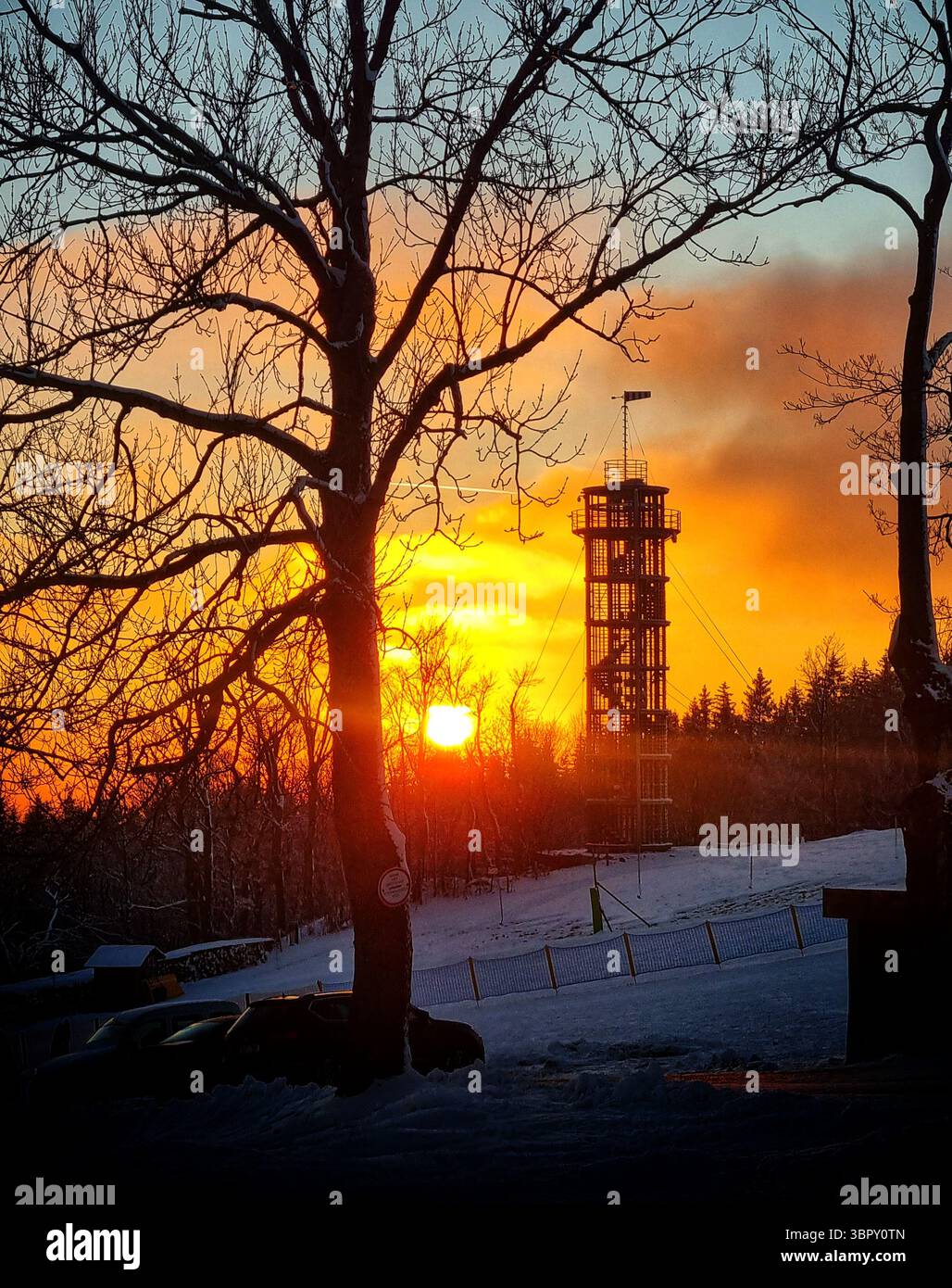 A lookout tower is perfectly silhouetted on a hilltop against the warm glow of a beautiful winter sunset on Christmas Day in the Czech mountains - Smartphone Captured Stock Image