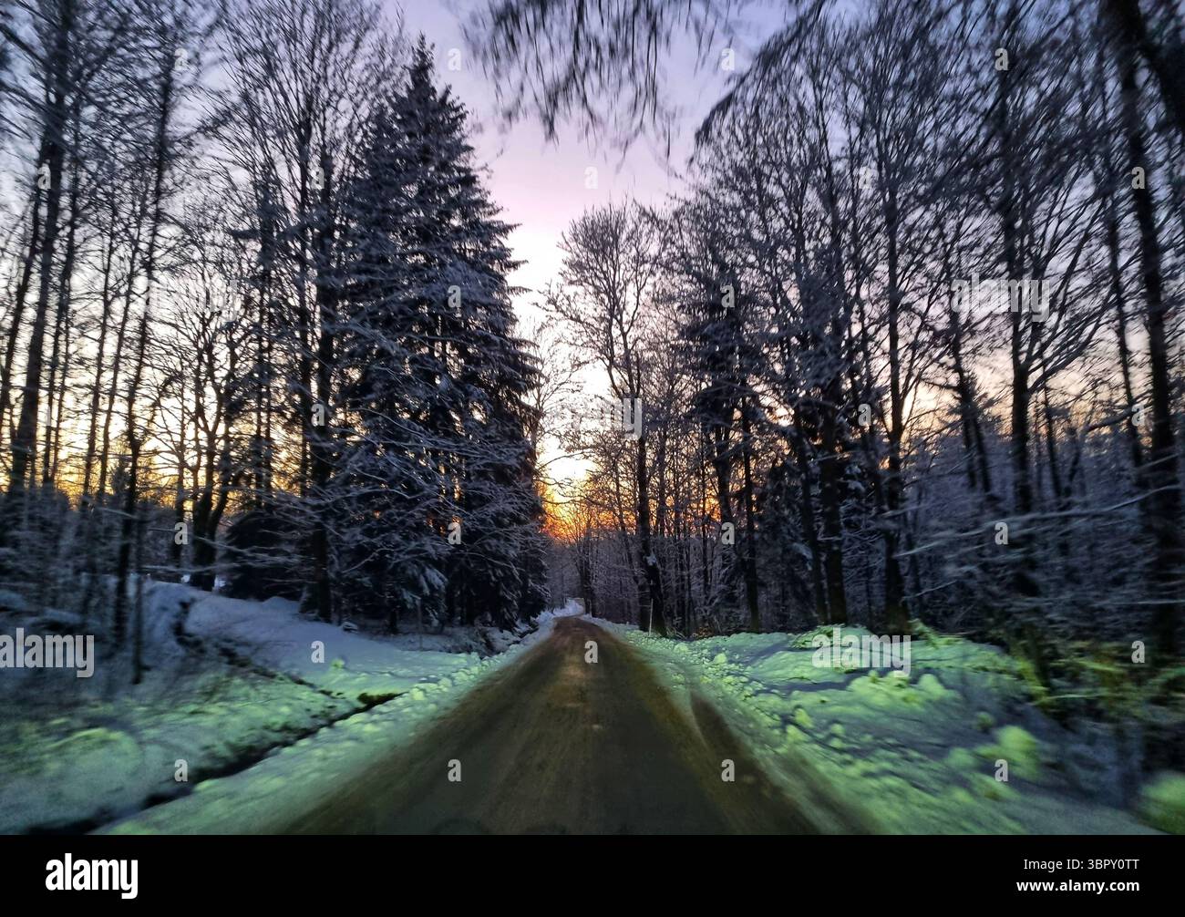 A remote country road with leading lines disappears into a dark and mysterious snowy evergreen forest during a moody winter twilight in the mountains. - Smartphone Captured Stock Image
