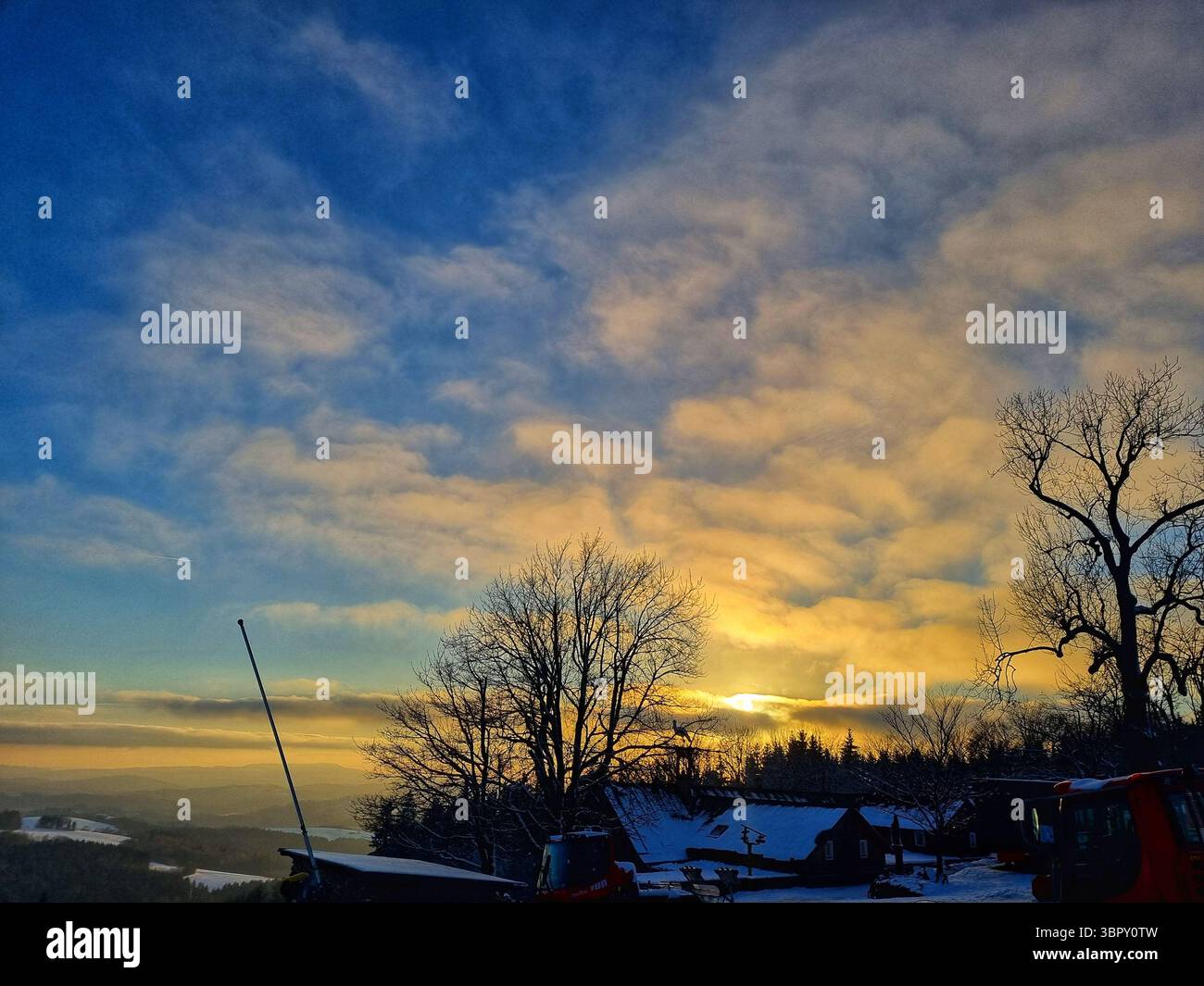 Atmospheric twilight sky filled with beautiful textured clouds in shades of blue and orange above a dark silhouetted forest landscape in the winter. - Smartphone Captured Stock Image