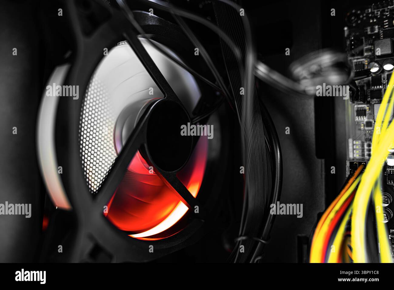 Computer's internal components featuring tangled wires and a glowing cooling fan illuminated by red-orange RGB lighting. Stock Photo