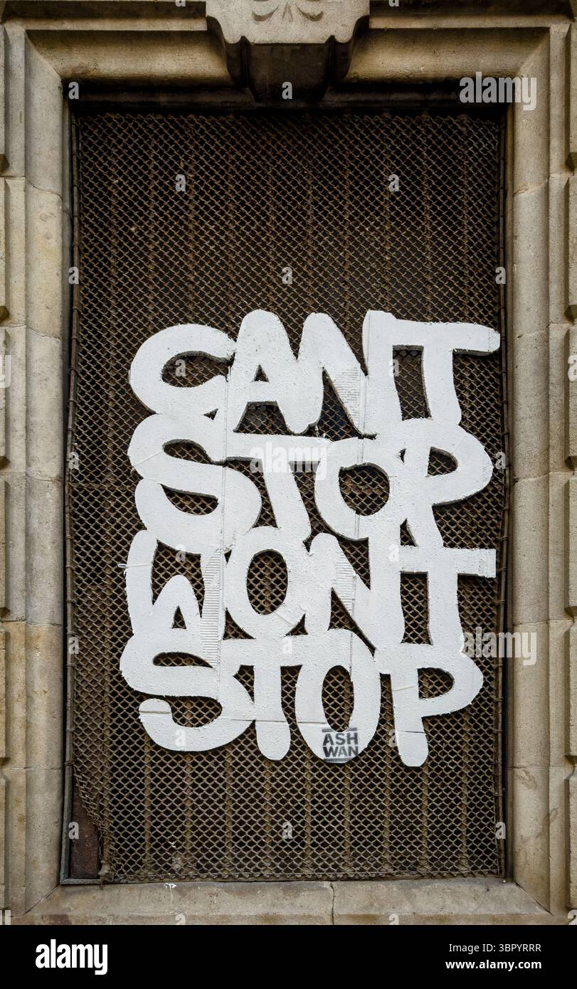 Graffiti style words with the message 'Can't Stop Won't Stop' on a wire mesh window grille in a stone window frame in Barcelona, Spain. Stock Photo