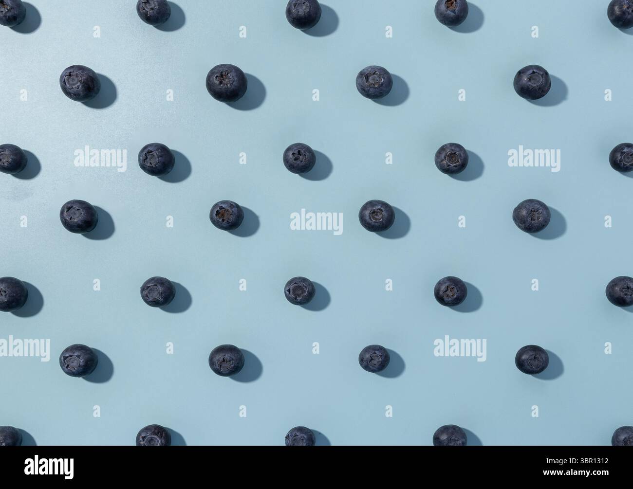 Blueberries forming a repeat pattern on a light blue background. Stock Photo