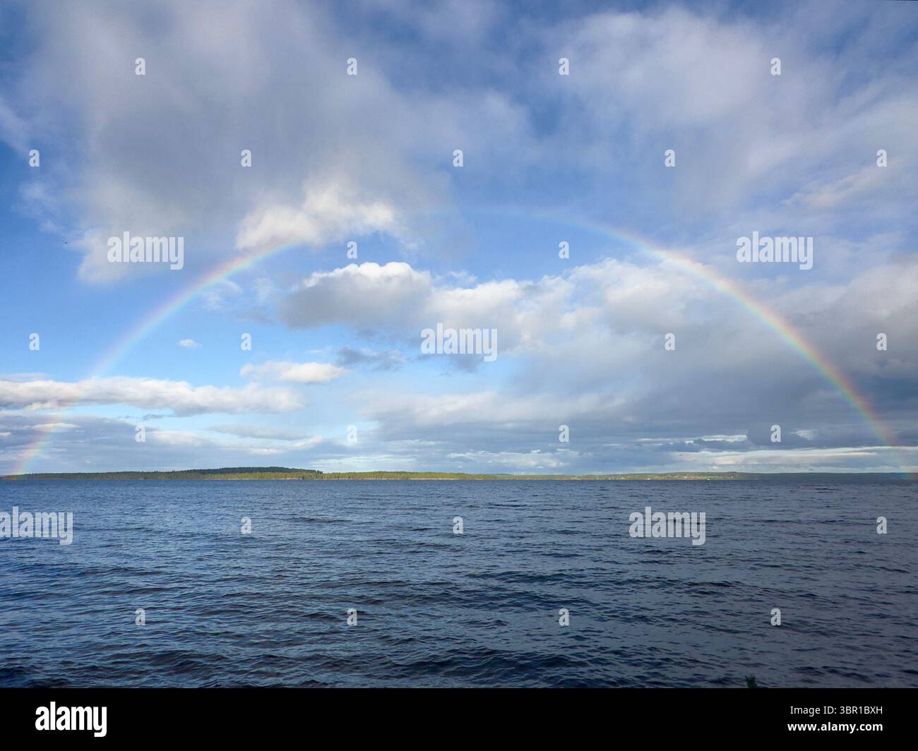 A stunning rainbow stretches across the sky above the calm ocean waters. - Smartphone Captured Stock Image