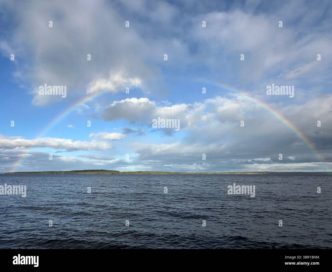 A stunning rainbow stretches across the sky above the calm ocean waters. - Smartphone Captured Stock Image