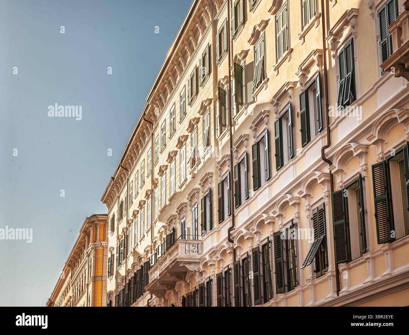 Late afternoon sunlight washes over an ornate 19th century residential block in Trieste's old town, arched windows and dark green shutters that open t Stock Photo