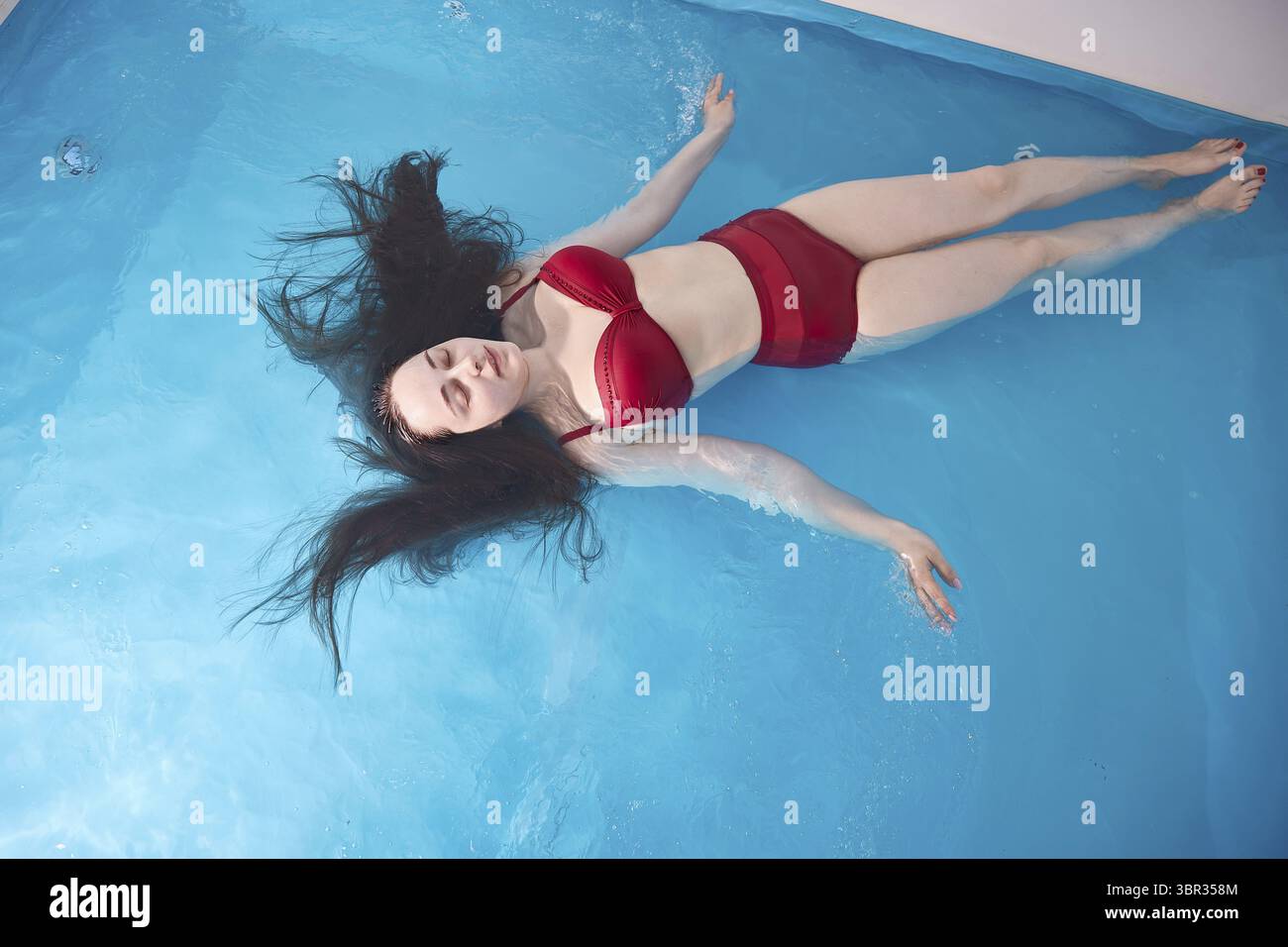 Eine junge Frau entspannt sich gerne in einem Schwimmbad oder einem Bad mit Salzwasser. Eine Bruenette mit offenem Haar entspannt sich in einem Wellne Stock Photo