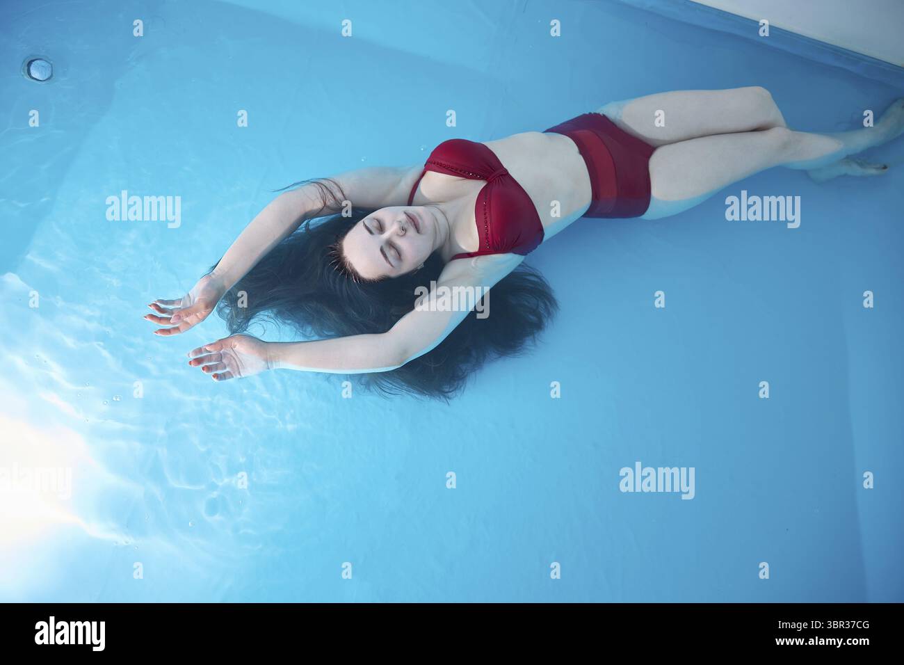 Eine junge Frau entspannt sich gerne in einem Schwimmbad oder einem Bad mit Salzwasser. Eine Bruenette mit offenem Haar entspannt sich in einem Wellne Stock Photo