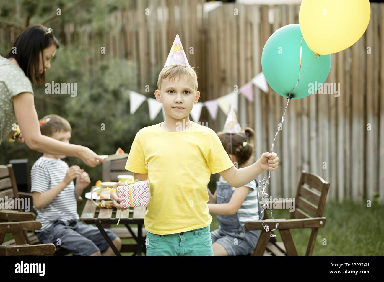 Niedlicher lustiger neunjaehriger Junge, der seinen Geburtstag mit Familie oder Freunden in einem Hinterhof feiert. Geburtstagsfeier. Kind traegt Part Stock Photo