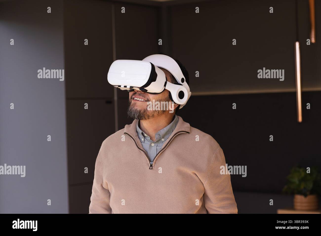 Senior Asian man wearing VR headset while standing under pendant light in modern lounge Stock Photo