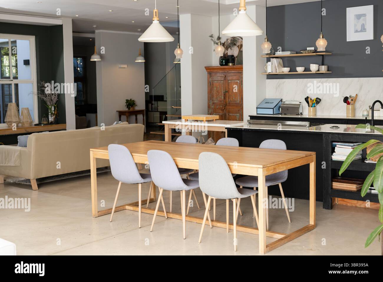 Wooden dining table featuring six grey chairs in open-plan living and dining with kitchen island ...