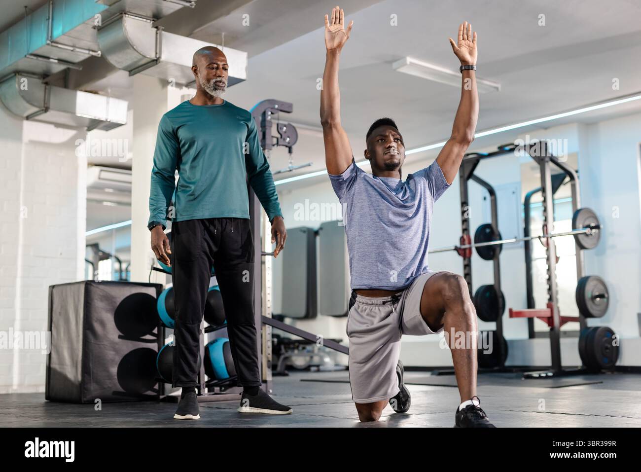 African American coach and client monitoring lunge form near squat rack ...