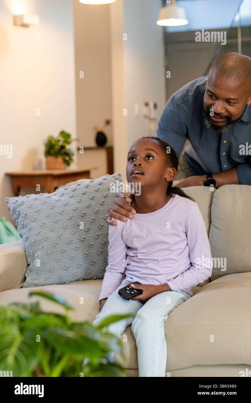 African American father and daughter sitting on sofa holding remote ...