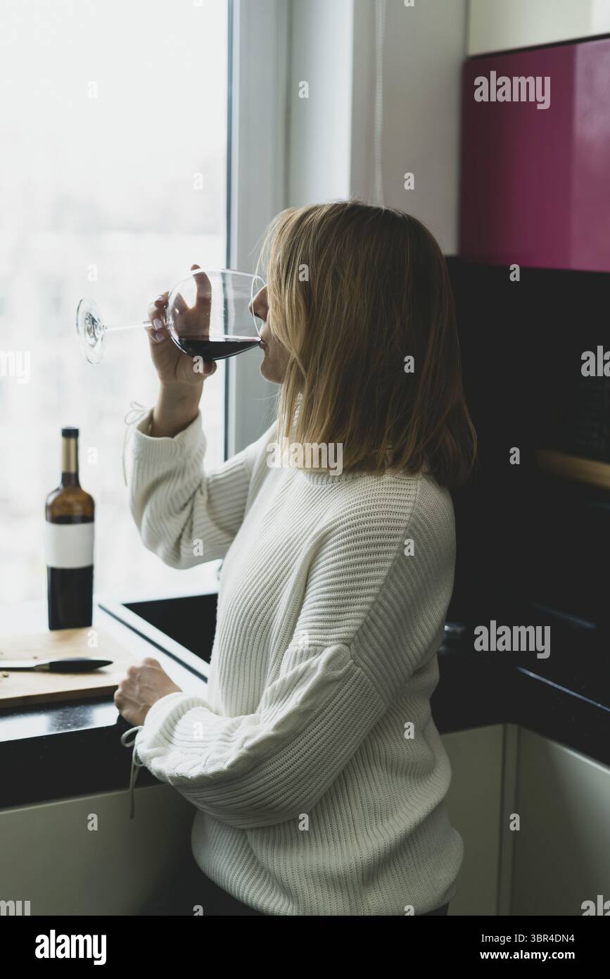 Happy young woman drinking wine in the kitchen at home Stock Photo