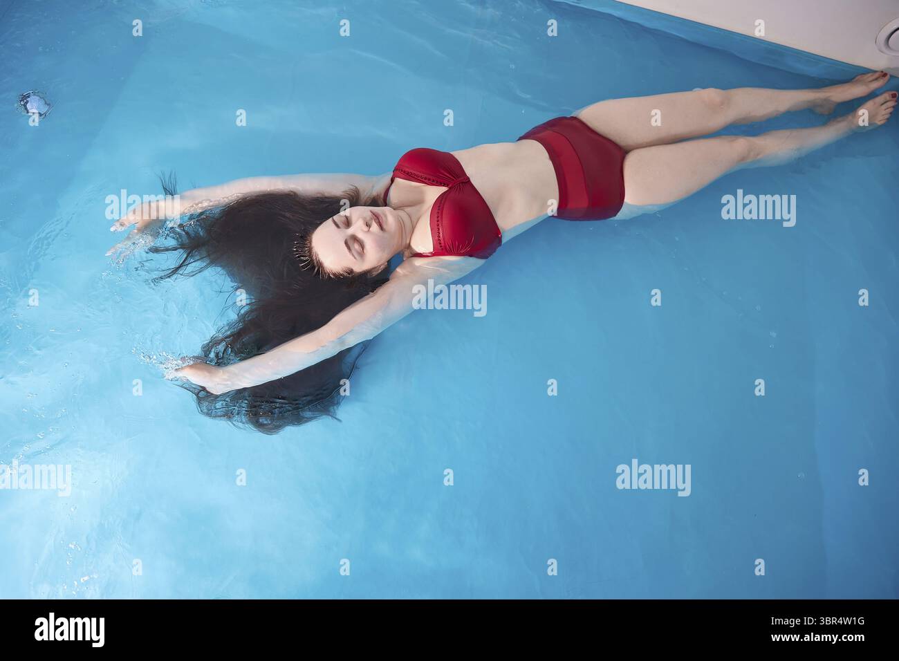 Eine junge Frau entspannt sich gerne in einem Schwimmbad oder einem Bad mit Salzwasser. Eine Bruenette mit offenem Haar entspannt sich in einem Wellne Stock Photo