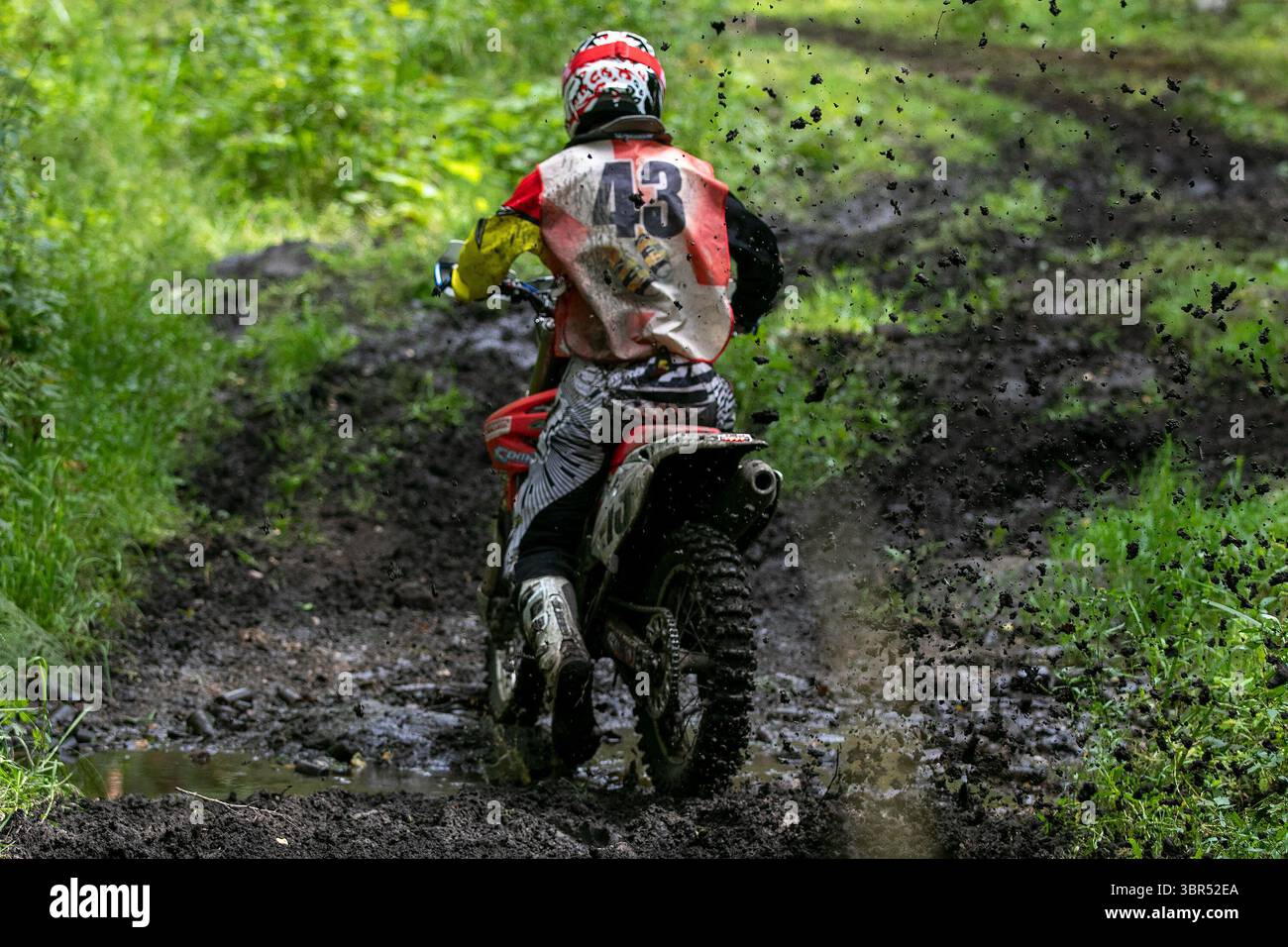 Rear view enduro rider on dirt bike speeding through wet muddy forest ...