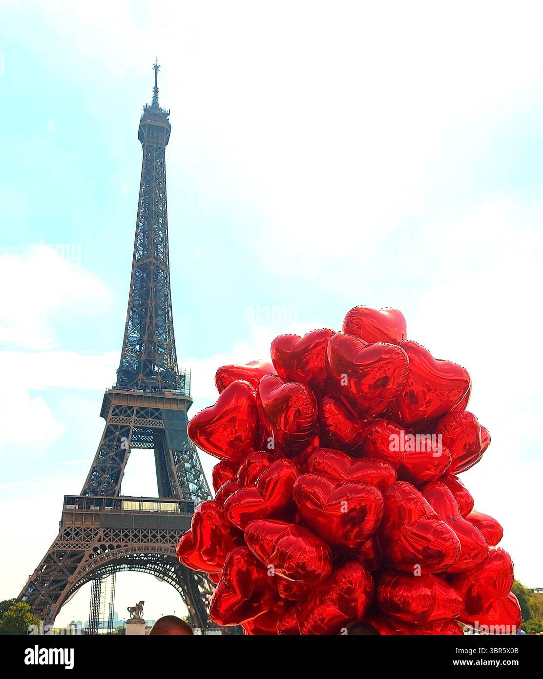A cheerful and romantic Paris scene in France, with the Eiffel Tower behind a vibrant cluster of red heart-shaped balloons. Stock Photo