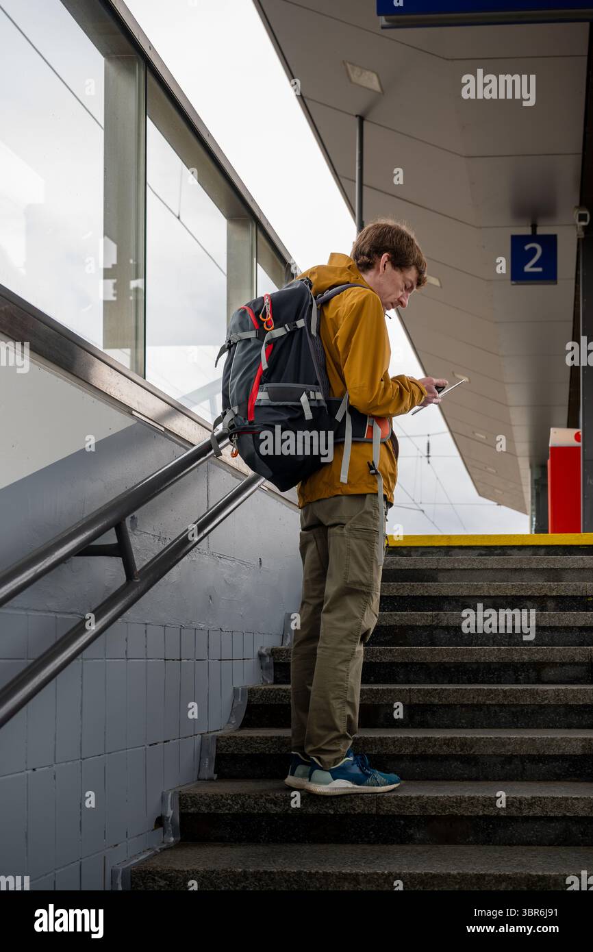 Man with backpack using smartphone at train station stairs Stock Photo