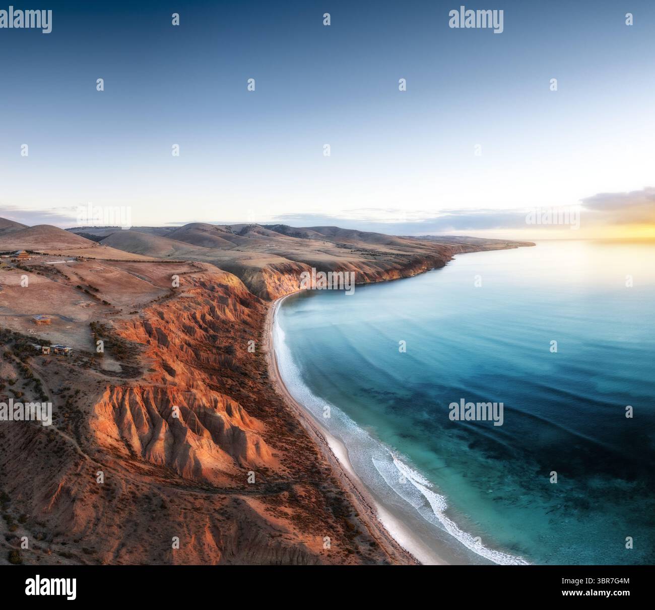 Aerial view of golden cliffs meet the turquoise sea under a serene sky ...