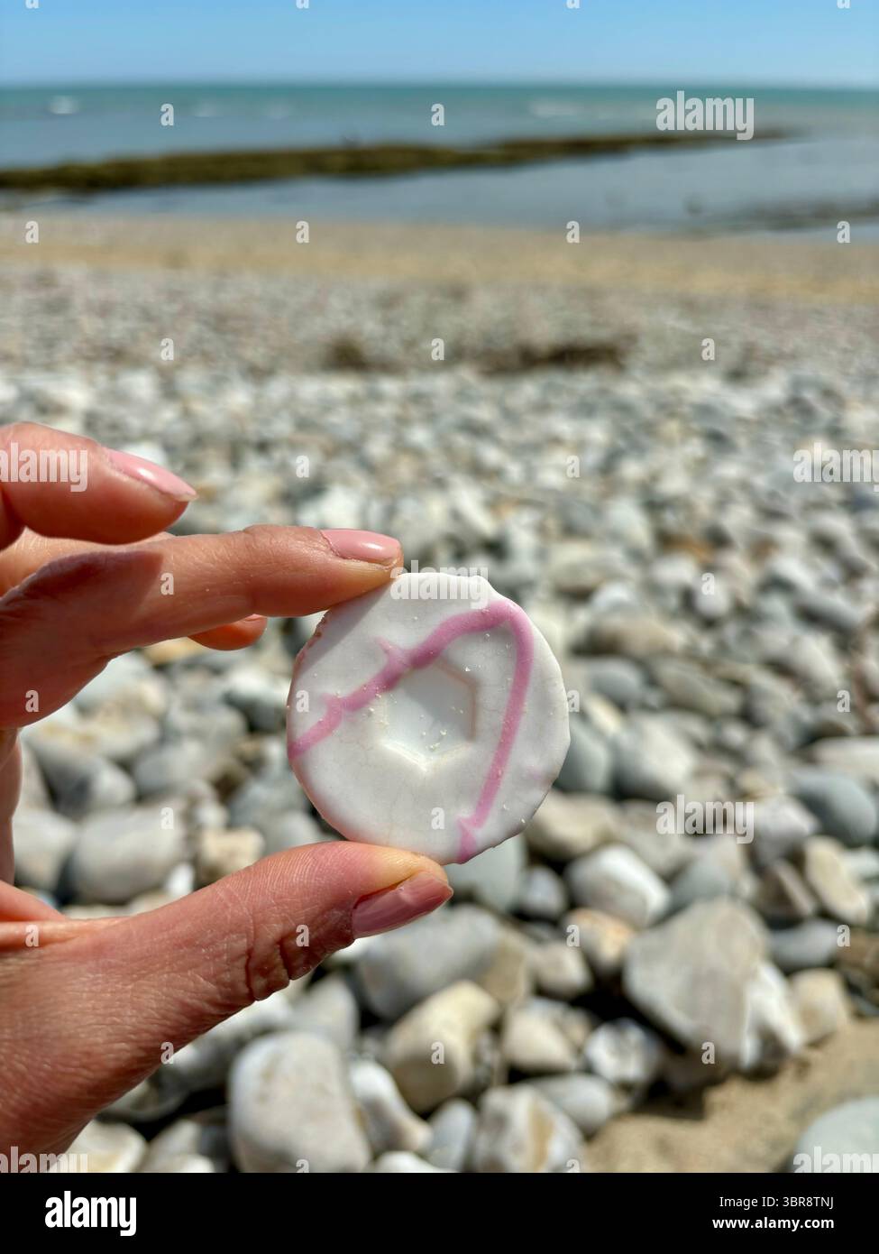 iced party ring biscuit being held up in front of pebbly beach - Smartphone Captured Stock Image