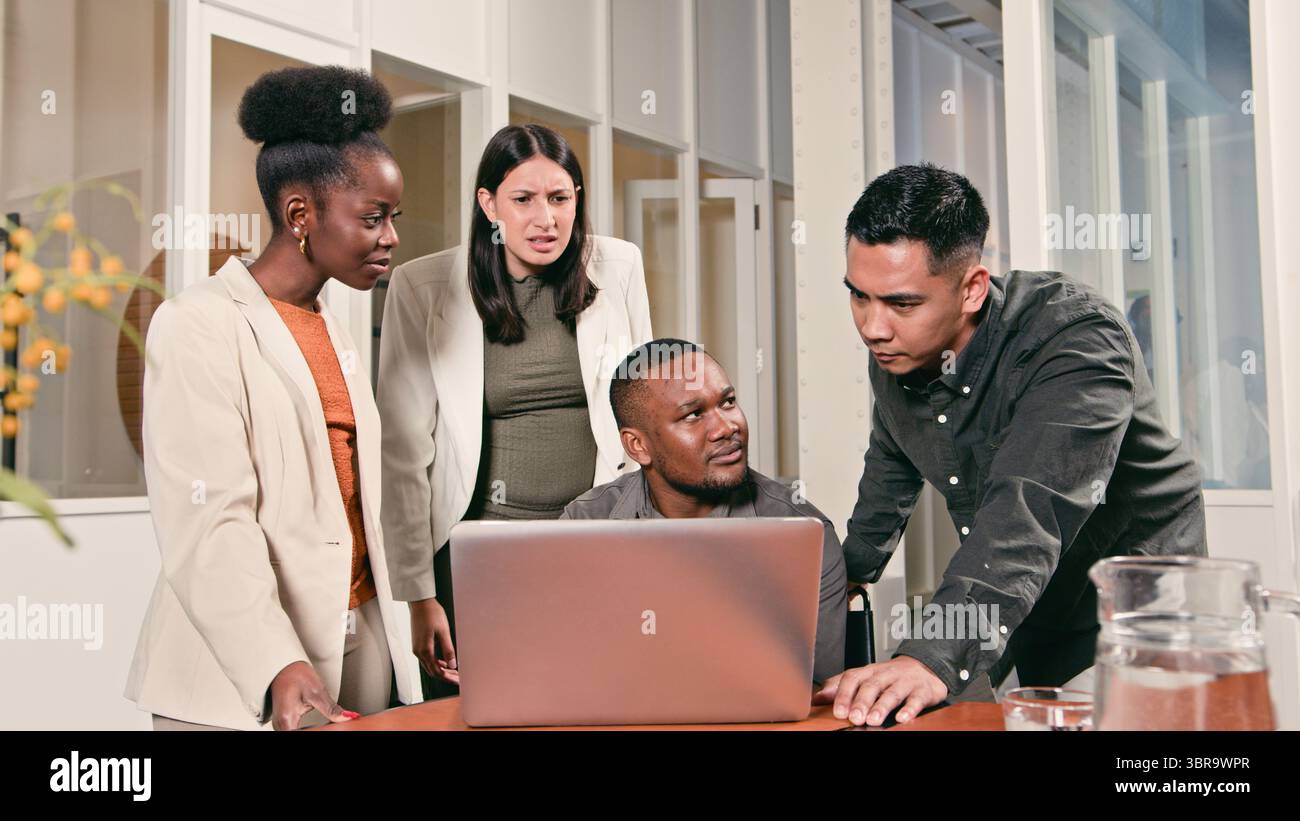 Diverse Team Collaborating Closely on a Project Using a Laptop in a Modern Office Setting Stock Photo