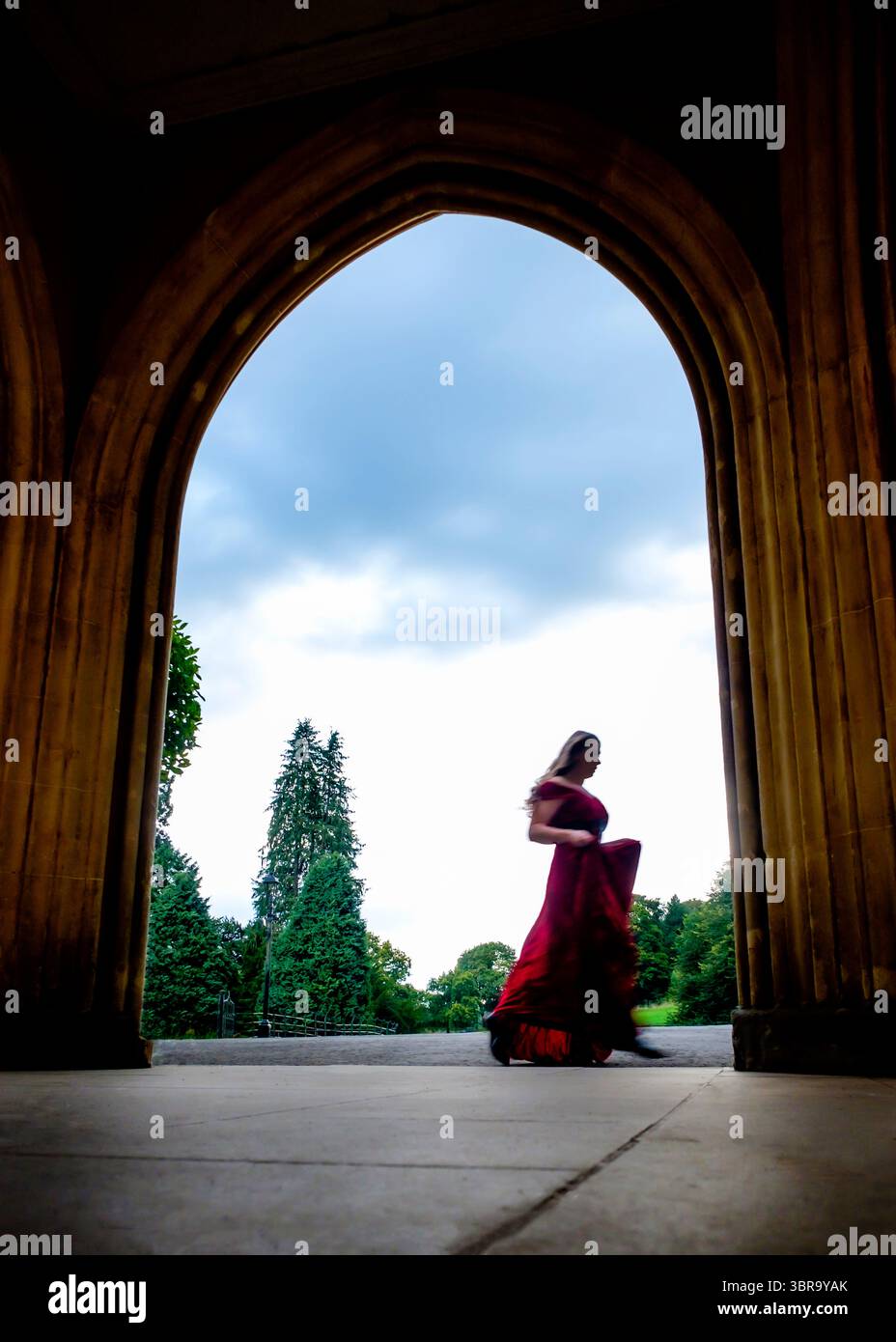 A woman in a red dress walks through an archway Stock Photo - Alamy