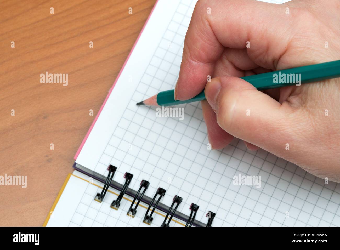 A person focuses on writing notes in a grid-patterned notebook. Stock Photo