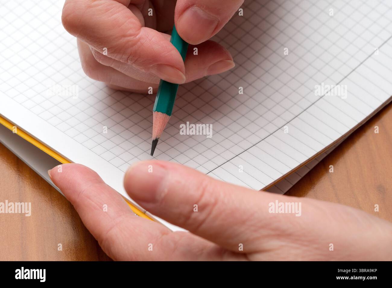A hand skillfully writes on grid paper using a green pencil, capturing thoughts. Stock Photo