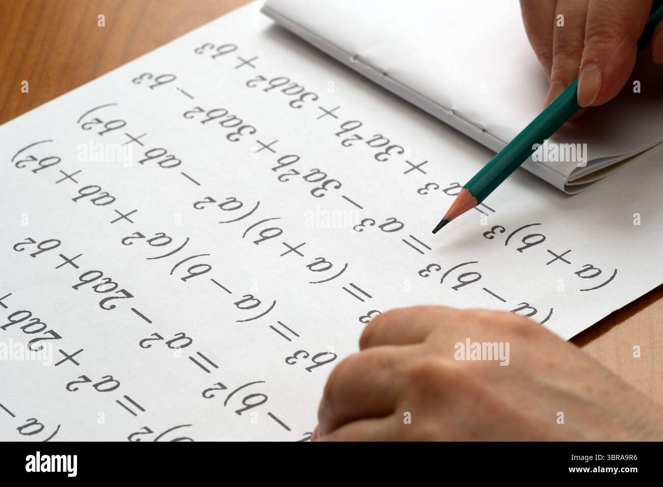 A person focuses on solving math problems with a green pencil, surrounded by notes. Stock Photo