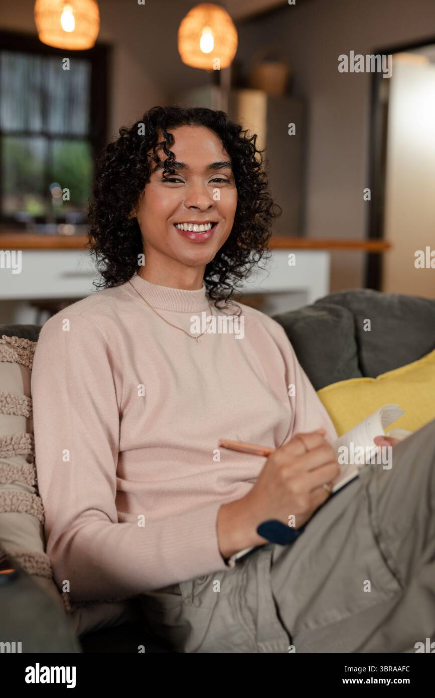 Non-binary person smiling and writing in notebook with pen on gray ...