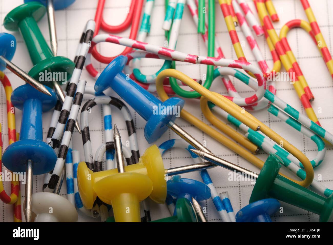 Various paper clips and push pins arranged haphazardly on graph paper ...